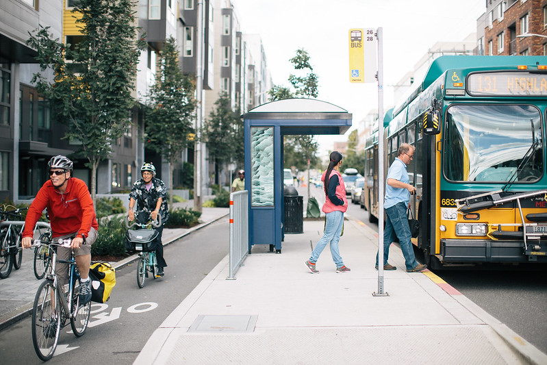 Cyclists ride past a bus stop as riders board the bus